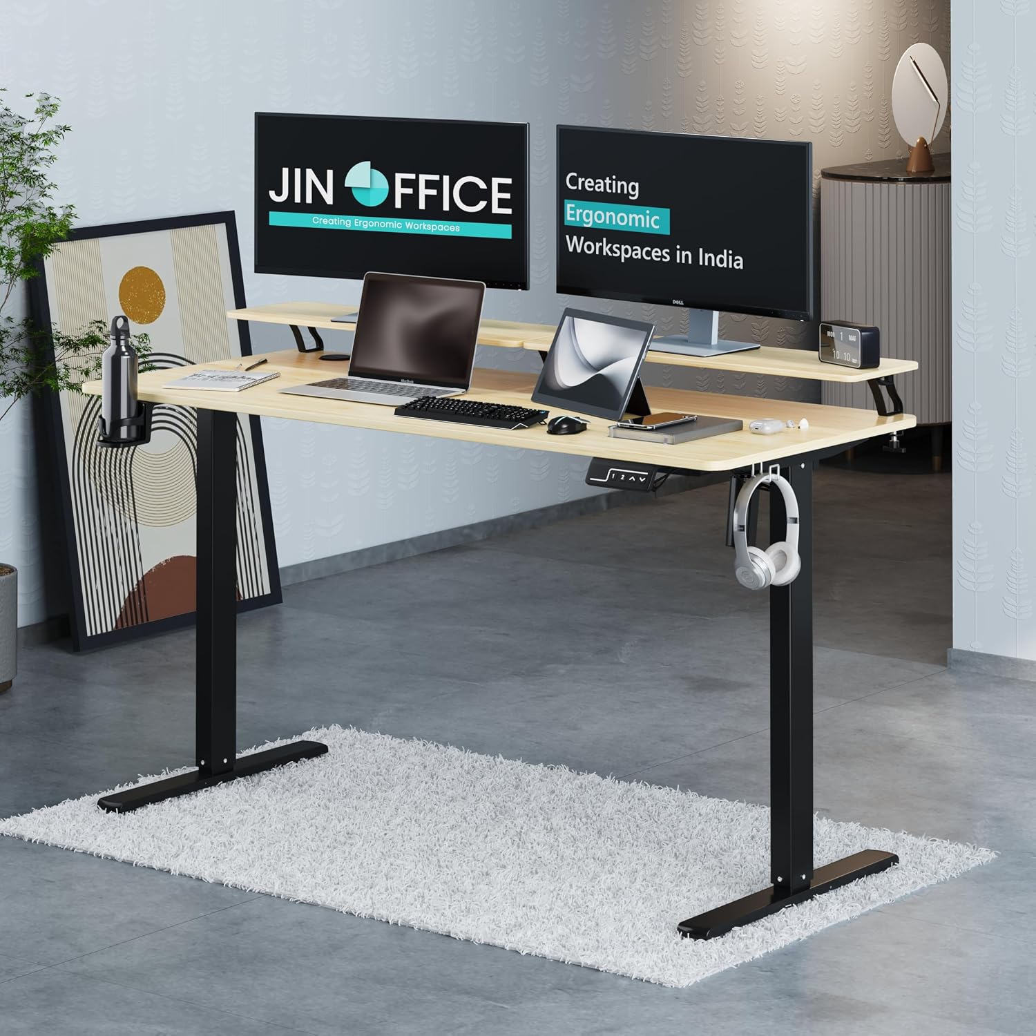 A JIN OFFICE standing desk with a light wood top and black metal legs, shown in a modern home office setup with two computer monitors, a laptop, headphones, and a white shag rug.